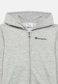 Γκρι φούτερ με φερμουάρ, φτιαγμένο από απαλό ύφασμα, διαθέτει φερμουάρ μπροστά, δύο πλαϊνές τσέπες και το λογότυπο Champion σε ναυτικό μπλε στο στήθος.