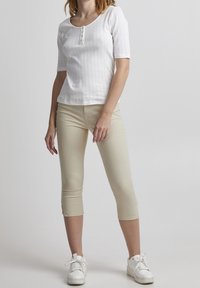 Biała bluzka z krótkim rękawem o teksturowanym wzorze i okrągłym dekoltem, z beżowymi spodniami 3/4 i białymi trampkami.