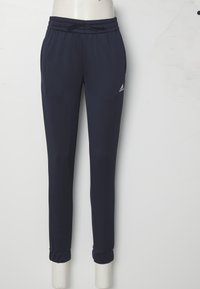 Námornícky modré športové nohavice z hladkej tkaniny. Majú elastický pás s šnúrkou a zúžené manžety. Logo Adidas na stehne.