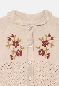 Vaalea beige neulecardigan, jossa on punaisia ja vihreitä kukkakirjontoja, ribbireunus kauluksessa ja helmipainikkeet. Zikzag-neulekuvio helman reunassa.