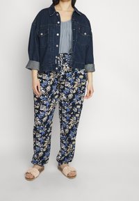 Denimjakke, mørkeblå, med to frontlommer og optrukne ærmer; parret med bukser med blomstermotiv i marineblå, creme og blå; lette sandaler.