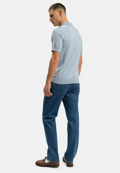 Ljusblå pikétröja med korta ärmar, ribbad fåll och nederkant, i kombination med mörkblå denimjeans och bruna flätade loafers.