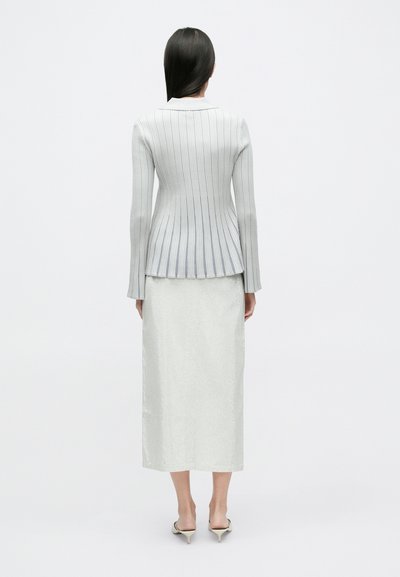 Svetlosivá rebrovaná pletená bunda so štruktúrovaným peplumom v páse, kombinovaná s bielou textúrovanou sukňou po kolená a špicatými vysokými opätkami.