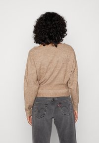 Stickad, beige tröja med avslappnad passform, bred rund halsringning och midjeband, ihop med mörkgrå högmidjade jeans med sydda fickor.