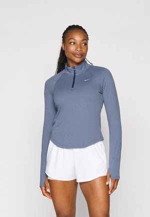 Langermet, kvart-zip genser i hederblått stoff med en glattere tekstur; har et Nike-logo på brystet og en buet kant.