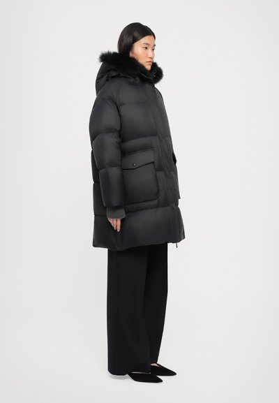 Black puffer coat with a detachable fur-trimmed hood, featuring a front zipper, side pockets, and a boxy silhouette. Smooth, matte finish.
