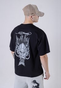Black short-sleeve T-shirt featuring a large grey dragon graphic on the back, with "Ed Hardy" text above. Light grey pants visible.