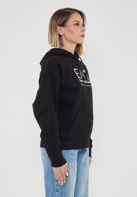 Felpa con cappuccio nera, dotata di tasca frontale e un design del logo bianco. Realizzata in materiale morbido, con maniche lunghe e polsini a costine.