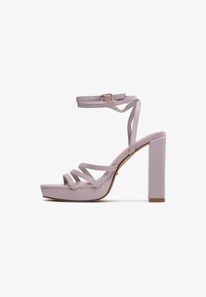 Sandalo con tacco alto a blocco color lilla, con cinturino alla caviglia e molteplici sottili cinturini sopra le dita, mostrato su sfondo bianco.
