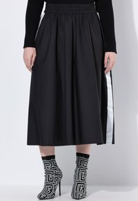 Jupe midi noire avec une bande latérale blanche, portée avec des bottes à talons hauts en chaussette à motif géométrique noir et blanc et un haut à manches longues noir.