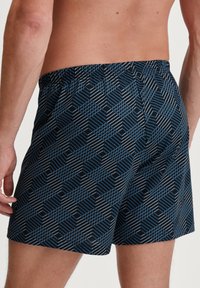 Zwemshorts in een donkerblauwe stof met een geometrisch patroon van in elkaar verstrengelde lijnen in lichtblauw en grijs. Elastische tailleband, lengte tot halverwege de dij.