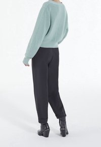 Mintgrön ribbad tröja i kombination med svarta avsmalnande byxor och svarta högklackade ankelboots, med en slät textur och avslappnad passform.