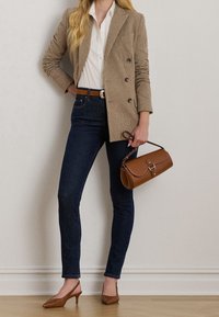Brązowa w kratkę podwójnie zapięta marynarka na białej koszuli, ciemne obcisłe dżinsy, brązowy pasek oraz brązowa torebka o sztywnej konstrukcji z zapięciem.