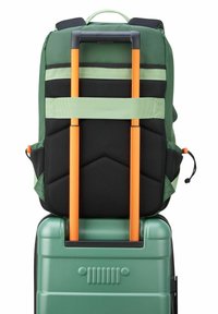 Mochila verde con acentos de malla negra, sujeta por correas naranjas sobre una maleta dura verde con textura lineal en la parte frontal.