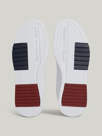 As solas brancas dos ténis apresentam um padrão em espinha de peixe texturizado. Os destaques incluem seções em azul escuro e vermelho na parte traseira com a marca "TOMMY JEANS" em relevo.