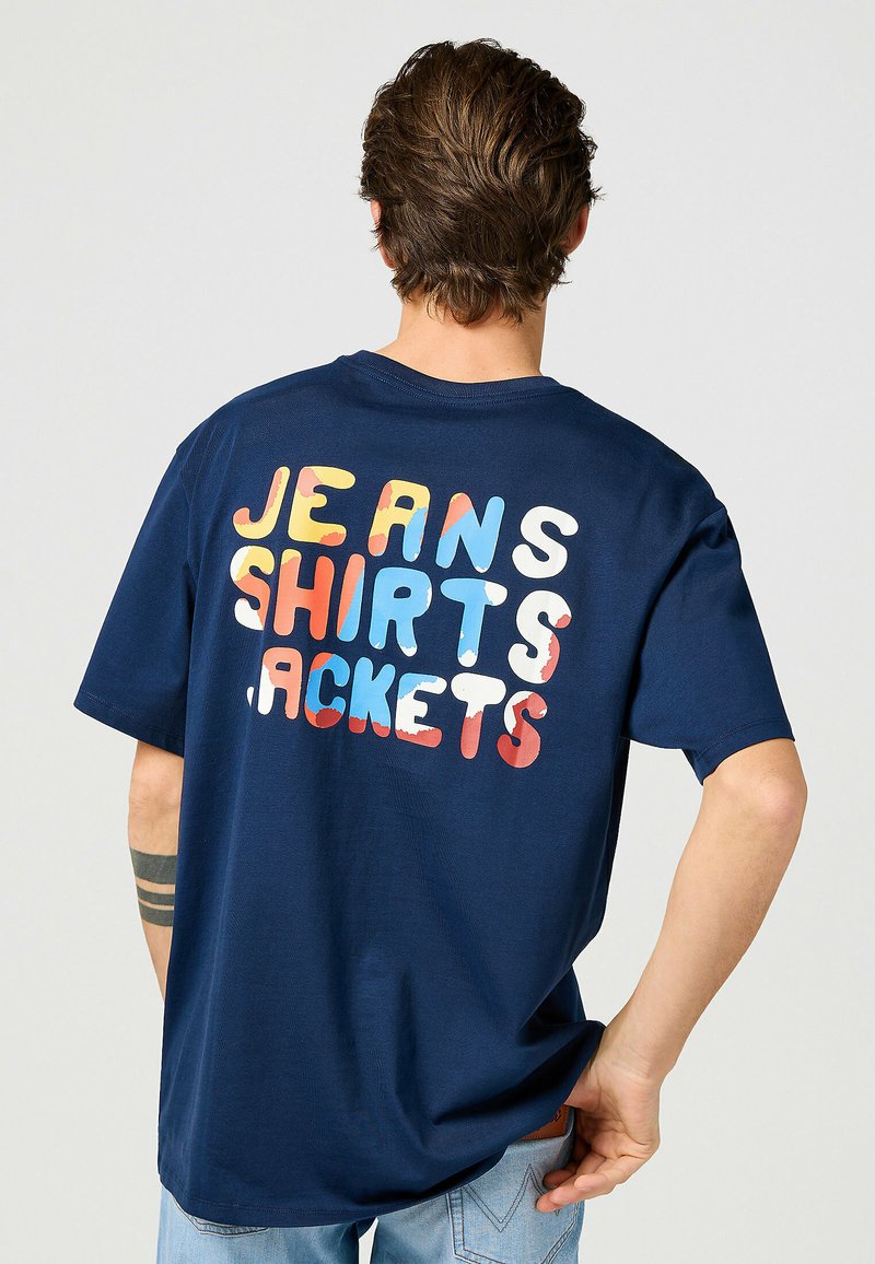 Mörkblå bomulls-T-shirt med flerfärgad text på baksidan som står "JEANS SKJORTOR JACKOR" i fet, rundad stil.