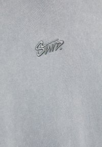 T-shirt en coton bleu clair avec un petit logo brodé "STWPD." en fil contrasté sur le devant. Surface en tissu tricoté texturé.