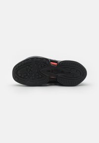 Semelle de sneaker noire avec des motifs de tread circulaires et linéaires, accents rouges légèrement visibles sur le dessus de la chaussure.