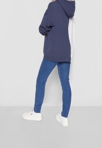 Felpa blu navy e grigia a blocchi di colore con un ampio cappuccio, abbinata a jeans skinny blu e sneakers bianche. Tessuto morbido e vestibilità comoda.