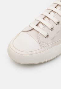 Beige lädersneakers med rundad tå, platta vita snören och metallöglor. Har detaljer i sömnad längs sidan och en gummisula.