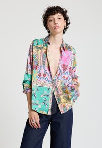 Collared, multi-patterned shirt featuring vibrant colors like pink, turquoise, and yellow, with floral and paisley designs, made of lightweight fabric.