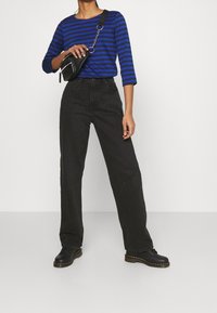 Camisa de manga larga a rayas azules y negras combinada con unos pantalones de tiro alto, anchos y negros, y botas negras con cordones. Pequeño bolso negro cruzado.