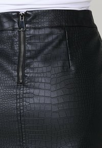 Zwarte faux leren rok met een gestructureerd krokodillenpatroon, voorzien van een ritssluiting aan de voorkant en een slanke silhouet.