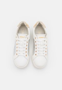 Vita sneakers med metallisk silverfärgade sidopaneler, gyllene öglor och en texturerad häl. Snören i vitt, med varumärke på tungan och sidan.