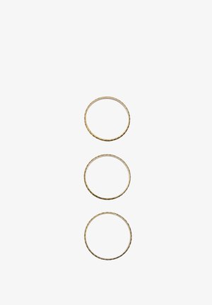 Trzy złocone metalowe pierścienie o różnych rozmiarach, z teksturowaną powierzchnią i subtelnymi różnicami w grubości.