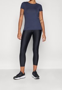 Camiseta atlética de manga corta en color navy, leggins ajustados negros y zapatillas deportivas negras. El conjunto presenta una textura suave con un diseño elegante.