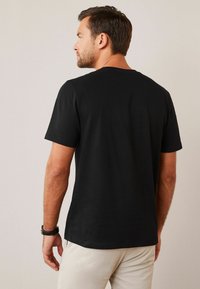 Camiseta de algodón negra con cuello redondo estándar, mangas cortas y una textura suave, que presenta un diseño liso sin patrones ni acentos.