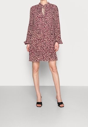 Abito con stampa leopardata in rosa chiaro e bordeaux, maniche lunghe, dettaglio con fiocco al collo, tessuto fluido e lunghezza a metà coscia, abbinato a mules nere con tacco.