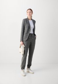 Grijze ruitjes blazer met bijpassende tapered broek, gedetailleerd met een trekkoord en zijstrepen. Gecombineerd met een wit topje en sneakers.