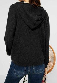 Tmavě šedá mikina s kapucí a volným střihem, s měkkou texturou a klokankovou kapsou. Kombinováno s modrými džíny.