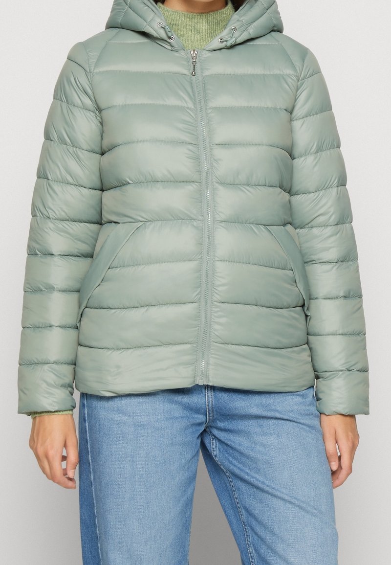 Lysegrøn dunjakke med lynlås foran, hætte og sidelommer. Har quiltede sektioner og en glat, blank tekstur.