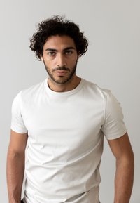 T-shirt bianca a maniche corte, design aderente, realizzata in tessuto liscio, con collo rotondo e dettagli delle cuciture minimi, indossata da un modello maschile.