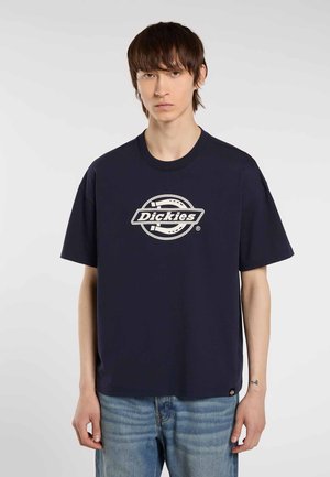 Camiseta de algodón azul marino con mangas cortas, que presenta un logo circular de Dickies en blanco y una etiqueta rectangular en el dobladillo. Corte casual.