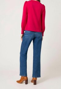 Fuchsia long-sleeve blouse featuring puffed shoulders, paired with high-waisted blue denim jeans and brown heeled ankle boots.