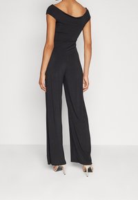 Schwarzer Jumpsuit mit schulterfreiem Design, langen, weiten Beinen und glatter Textur. Er verfügt über ein körperbetontes Oberteil und Rückendetails.