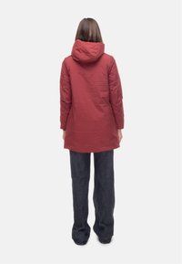 Giacca rossa con cappuccio dal design snodato, realizzata in tessuto liscio. Il retro presenta un orlo leggermente più lungo e maniche affusolate.
