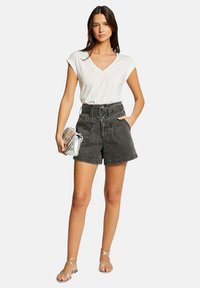 Pantalones cortos de mezclilla negra de cintura alta con un cinturón, combinados con una camiseta blanca de escote en V. Los accesorios incluyen un bolso de mano transparente y sandalias con tiras.