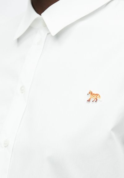 Biele button-up košele s malým, vyšitým oranžovým logom líšky na ľavej hrudi. Hladká tkanina s klasickým dizajnom goliera.