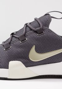 Sportskor med grå mesh-övre, förstärkt snörningssystem, guldig Nike-swoosh, texturerad vit mellansula och gummiyttersula för grepp.