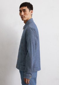 Leren spijkerjack in lichtblauw, met een kraag, knopen, een enkele borstzak en lange mouwen met knoopmanchetten. Uitgebreid ontwerp.