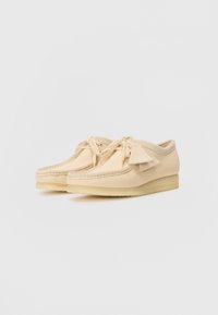 Scarpe in suede beige chiaro con punta tonda, frange decorative e lacci sulla parte anteriore. Presentano una suola in gomma texturizzata per una buona aderenza.