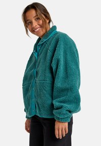 Teal fleece jas met een kraag, knoopsluiting en lange mouwen. Heeft een gestructureerde, zachte oppervlakte en contrasterende voering.