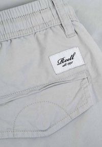 Pantalones cortos gris claro de algodón, con una cintura elástica, un bolsillo trasero con detalle de costura y una etiqueta de marca blanca.