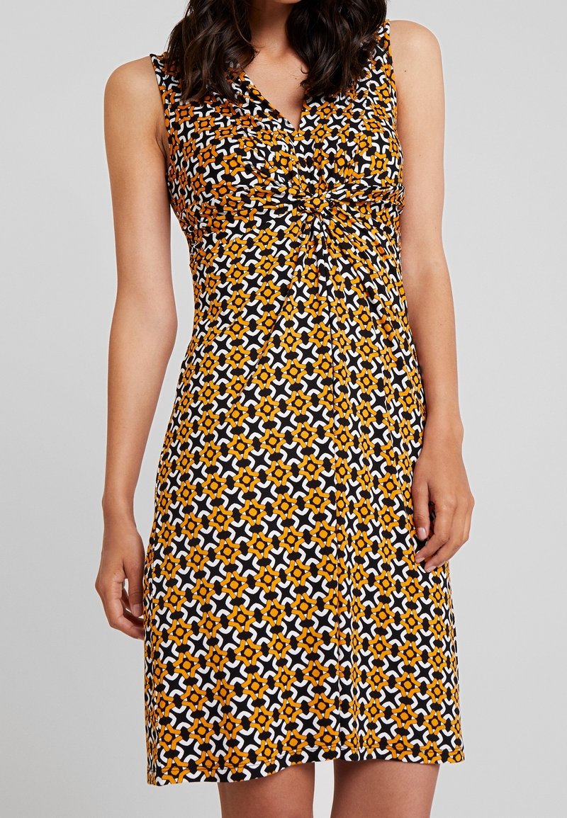 Vestido sin mangas con diseño de escote en V, que presenta un patrón floral en negro, naranja y blanco. Tejido suave con un detalle anudado en la parte delantera.