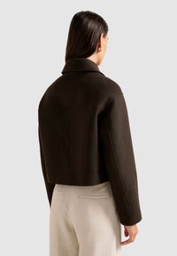 Bruine cropped jasje van textuurstof, met een klassieke kraag en gestructureerde schouders, gecombineerd met beige broek.