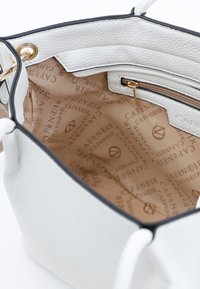 Hvid læderhåndtaske med tekstureret finish, der indeholder et beige interiør med et logo-mønster og en lynlåslomme.